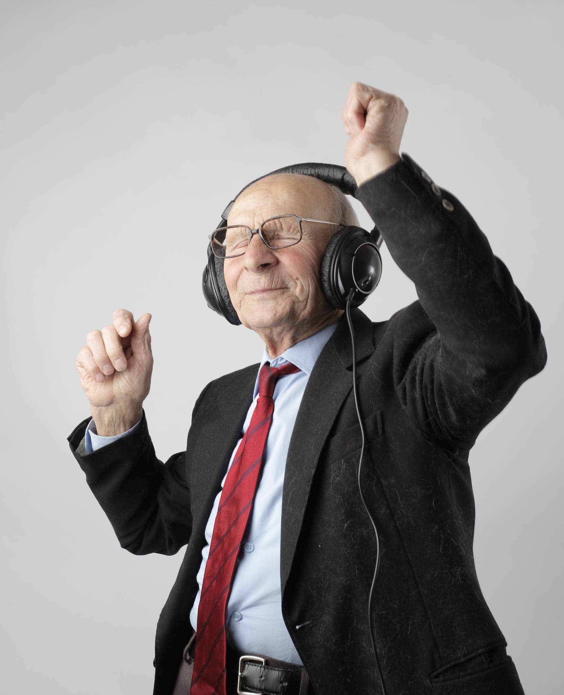 An older man in a suit and tie is listening to music.