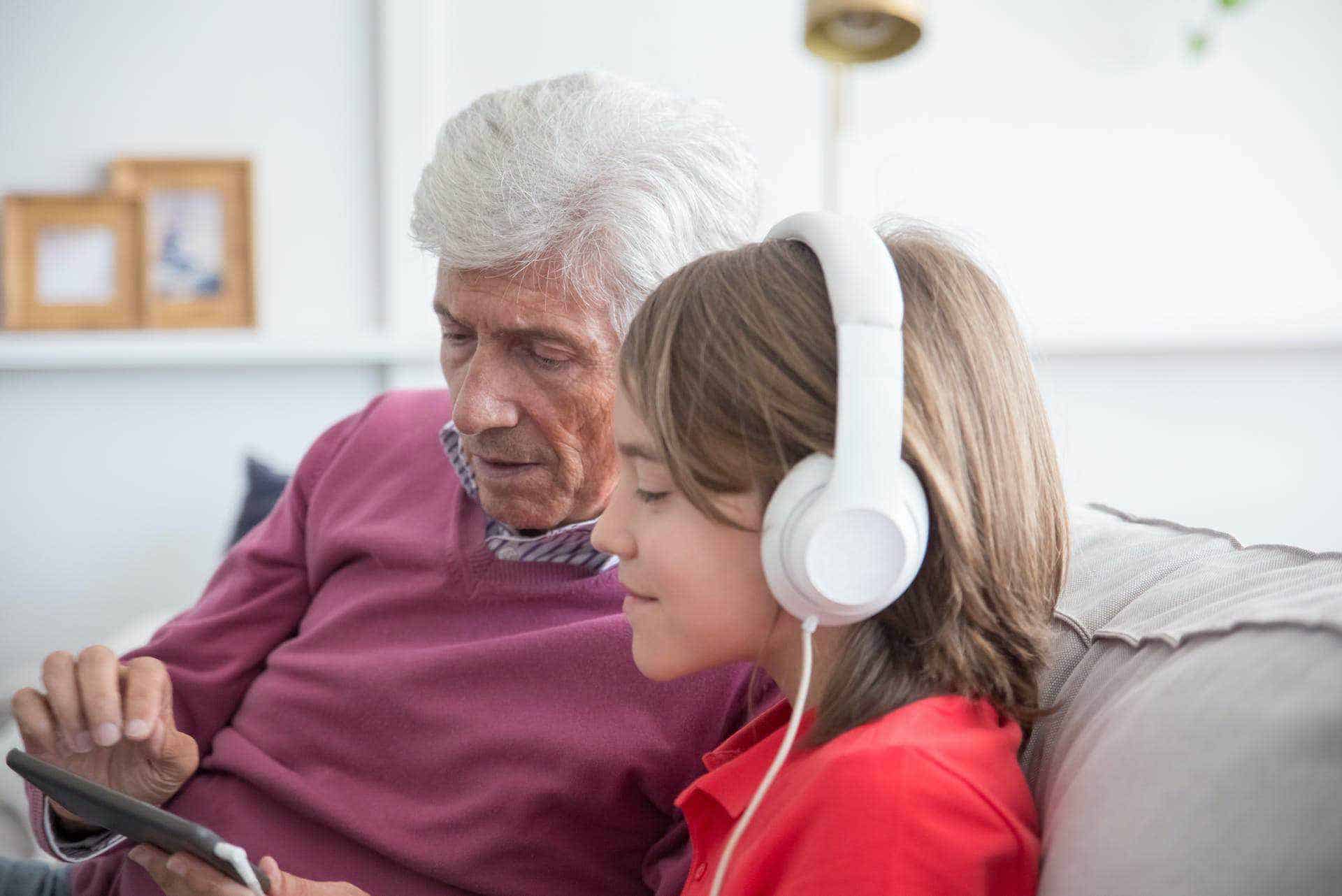 An older man and a young boy sitting on a couch with headphones on.